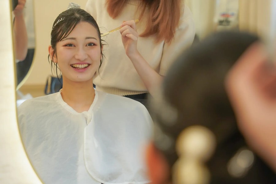 鹏越しにスタッフがメイク中、お客様が笑顔